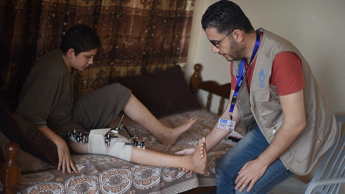 Ahmed sur son lit chez lui, avec un membre de l’équipe de Handicap International