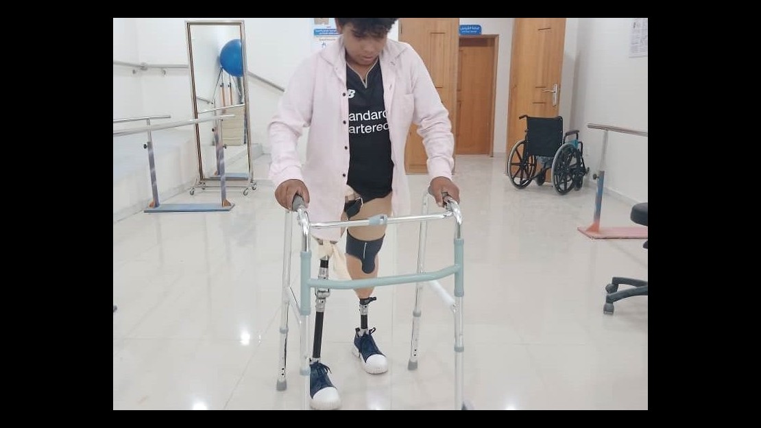 Au Yémen, un jeune garçon s'entraîne à marcher avec des prothèses en s'aidant d'un déambulateur.