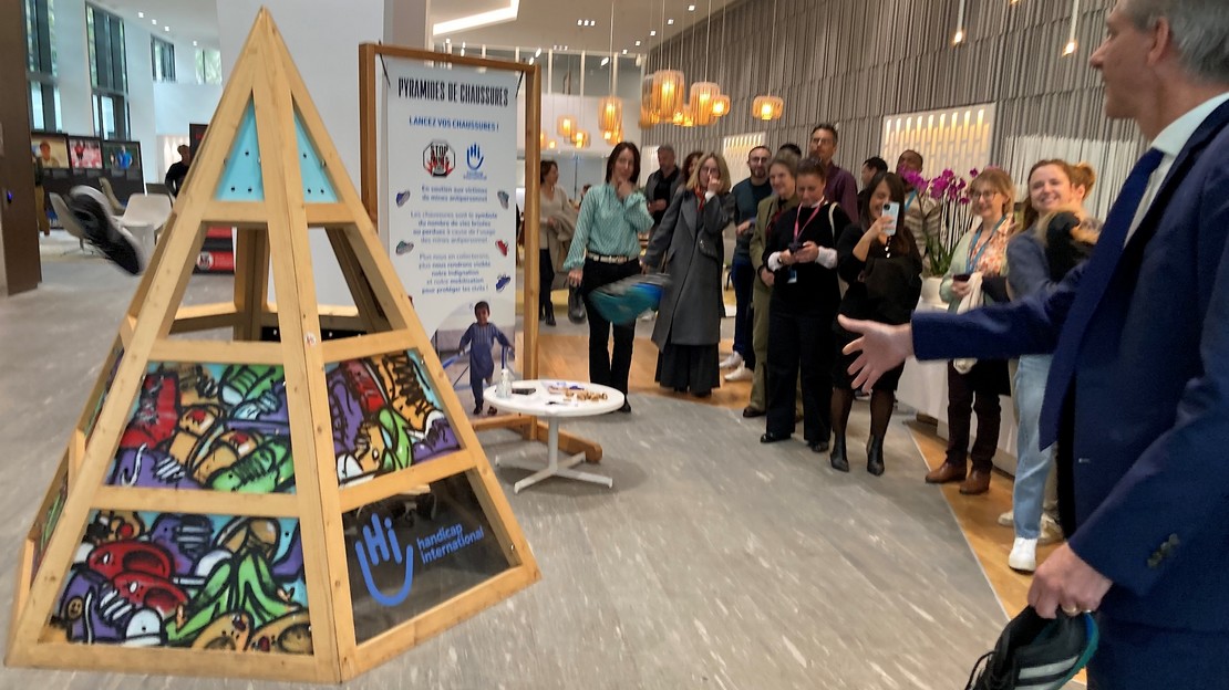 Devant plusieurs personnes, un homme lance une chaussure sur la Pyramide de Handicap International organisée dans l'entreprise Artelia.